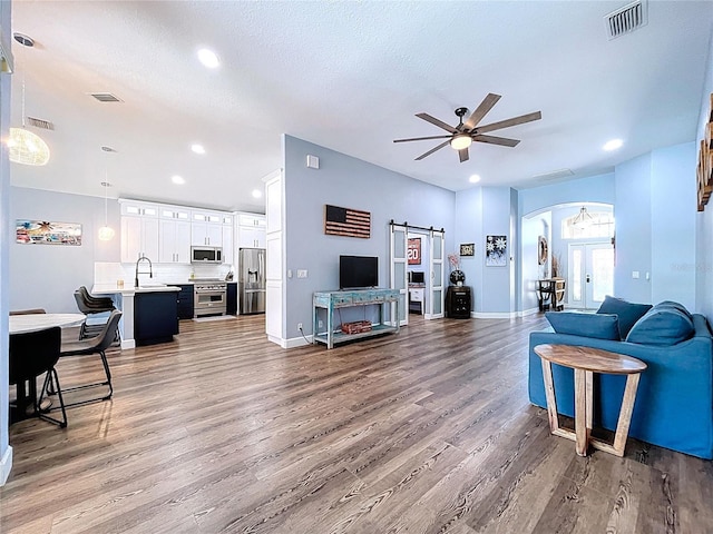 living room with visible vents, wood finished floors, ceiling fan, and a barn door