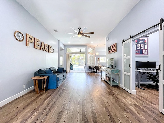 living room with a barn door, wood finished floors, visible vents, and ceiling fan