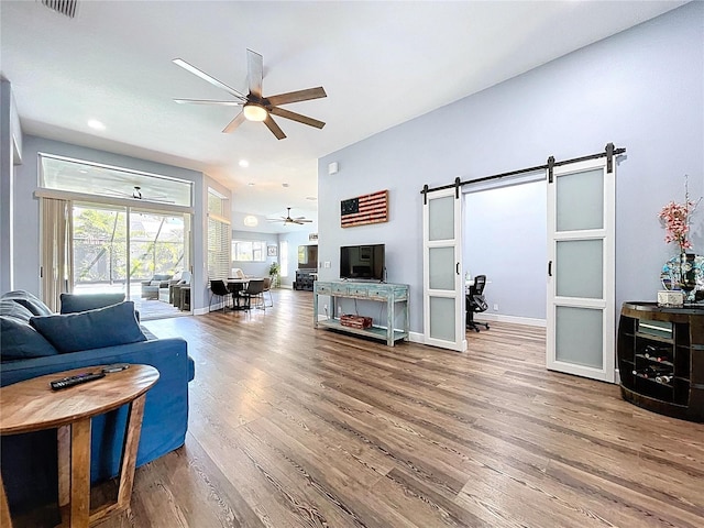 living room with a barn door, wood finished floors, baseboards, and ceiling fan