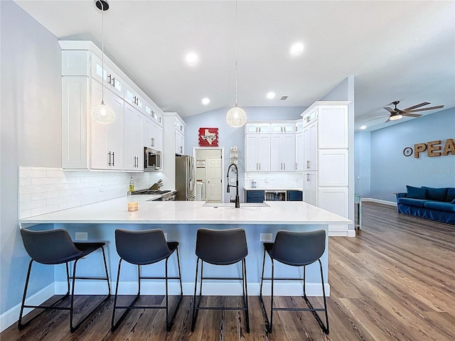 kitchen with a sink, dark wood-style floors, appliances with stainless steel finishes, a breakfast bar area, and a peninsula