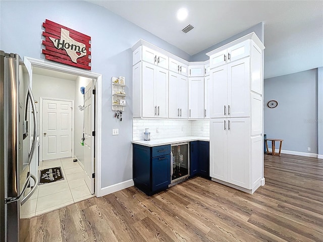 kitchen with visible vents, beverage cooler, blue cabinetry, white cabinetry, and stainless steel fridge