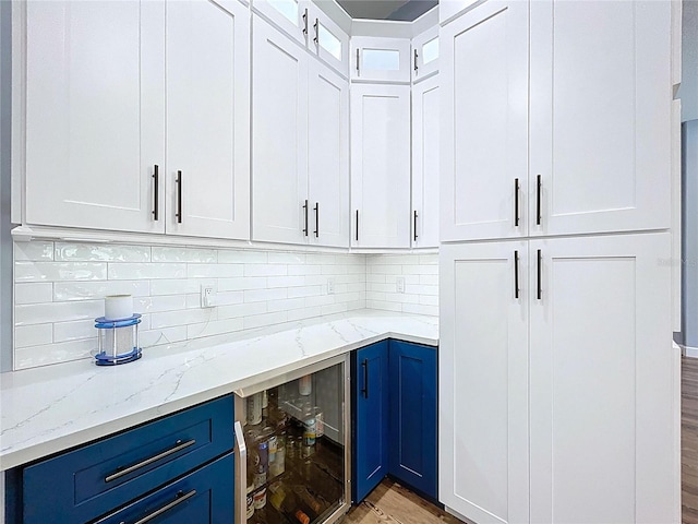 bar featuring light wood-style flooring, backsplash, and beverage cooler