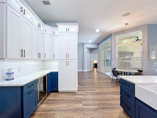 kitchen with backsplash, visible vents, blue cabinetry, and light wood-style flooring