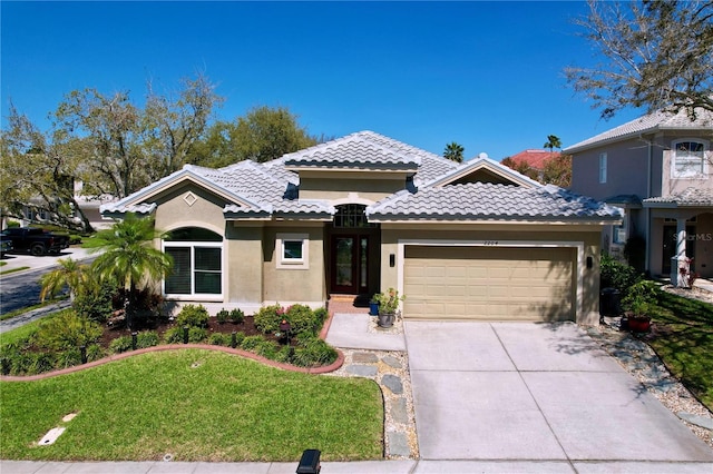 mediterranean / spanish-style home with a front yard, stucco siding, concrete driveway, a garage, and a tiled roof