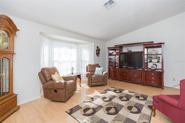 living area with a textured ceiling, visible vents, light wood-style floors, and vaulted ceiling