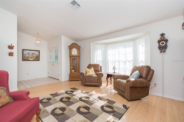 living room featuring lofted ceiling, wood finished floors, visible vents, and baseboards