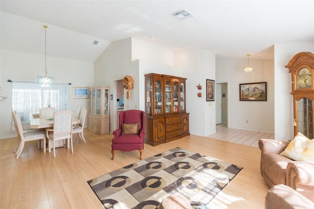 living area with a chandelier, visible vents, light wood finished floors, and high vaulted ceiling