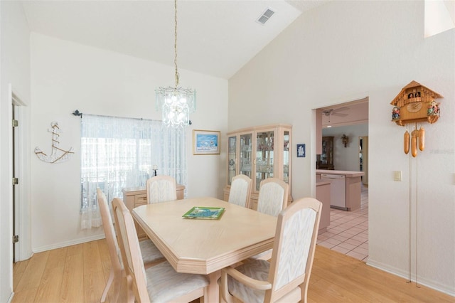 dining space featuring light wood-style flooring, ceiling fan with notable chandelier, visible vents, and high vaulted ceiling