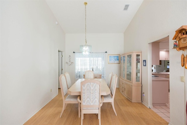 dining area featuring visible vents, baseboards, a chandelier, a high ceiling, and light wood-style floors