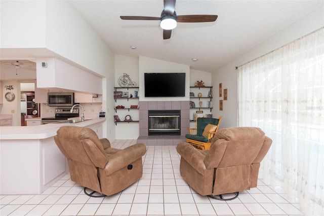 living area with a tiled fireplace, lofted ceiling, light tile patterned flooring, and ceiling fan