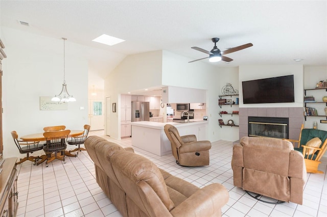 living area featuring a tiled fireplace, visible vents, ceiling fan with notable chandelier, and light tile patterned flooring