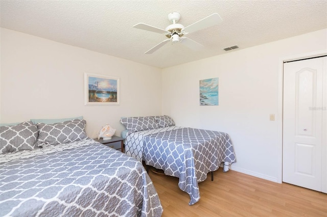 bedroom with a ceiling fan, baseboards, wood finished floors, visible vents, and a textured ceiling