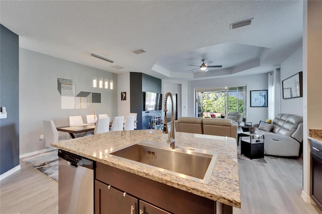 kitchen with light wood finished floors, visible vents, a tray ceiling, stainless steel dishwasher, and a sink