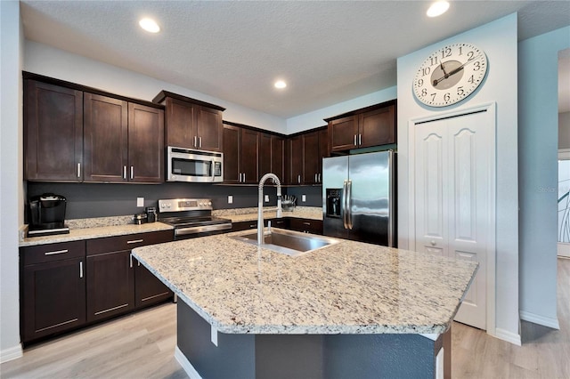 kitchen featuring light wood-type flooring, a sink, light stone counters, dark brown cabinetry, and appliances with stainless steel finishes