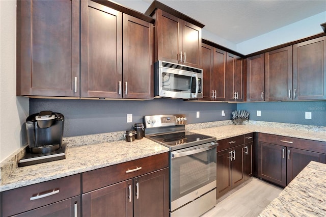 kitchen featuring dark brown cabinets, appliances with stainless steel finishes, light wood-type flooring, and light stone countertops