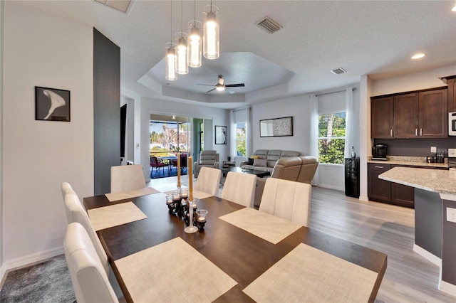 dining area featuring a tray ceiling, light wood-style floors, visible vents, and a healthy amount of sunlight