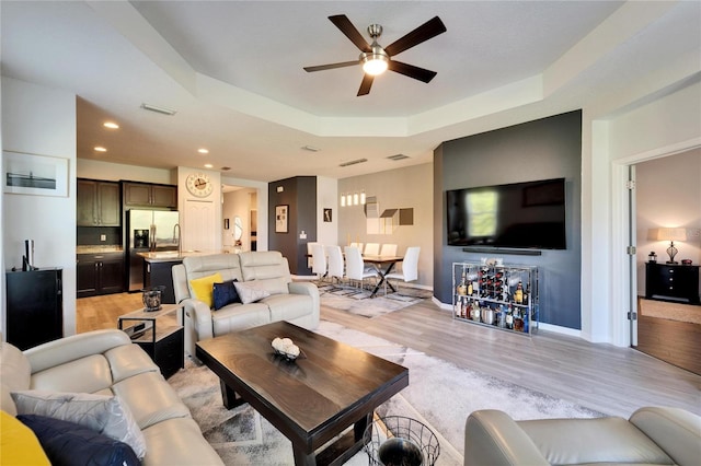 living room with a tray ceiling, visible vents, baseboards, and light wood finished floors