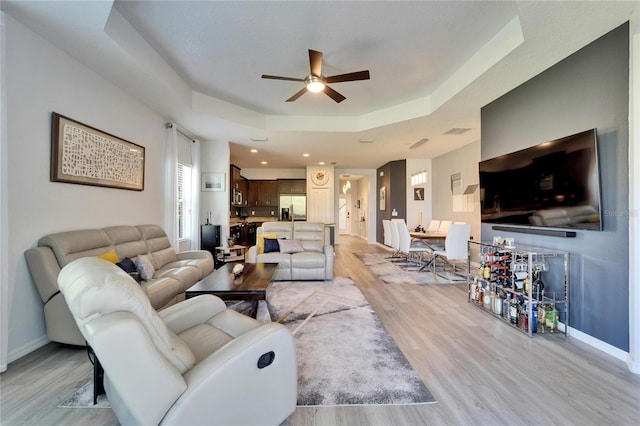 living area with visible vents, ceiling fan, baseboards, light wood-type flooring, and a tray ceiling