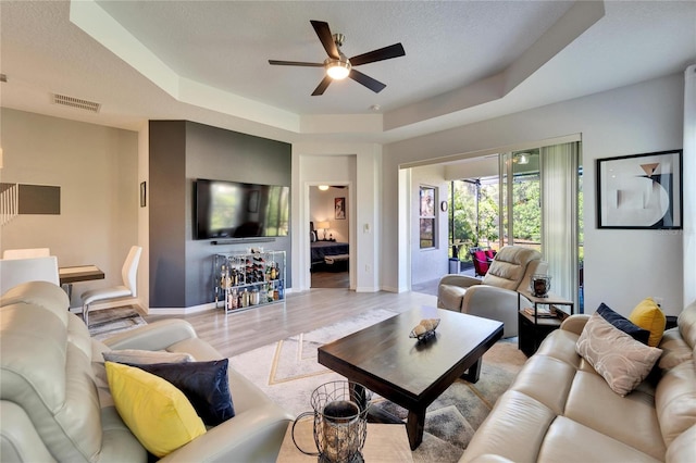 living area with baseboards, visible vents, light wood-style floors, a textured ceiling, and a raised ceiling