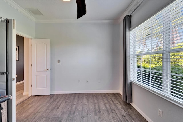 spare room featuring wood finished floors, visible vents, baseboards, ceiling fan, and crown molding