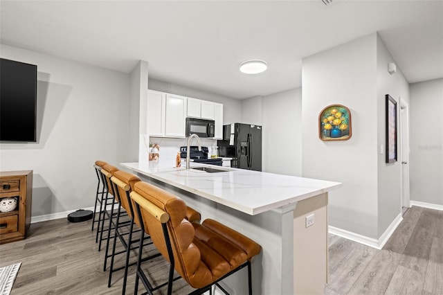 kitchen featuring a peninsula, light wood-style flooring, a sink, black appliances, and a kitchen breakfast bar