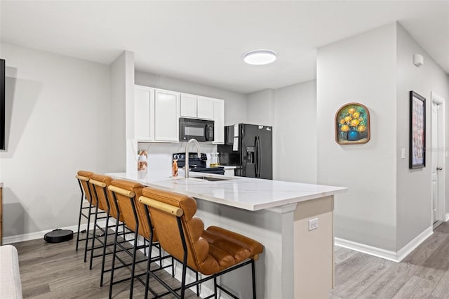 kitchen with a kitchen bar, black appliances, a peninsula, and light wood-style floors