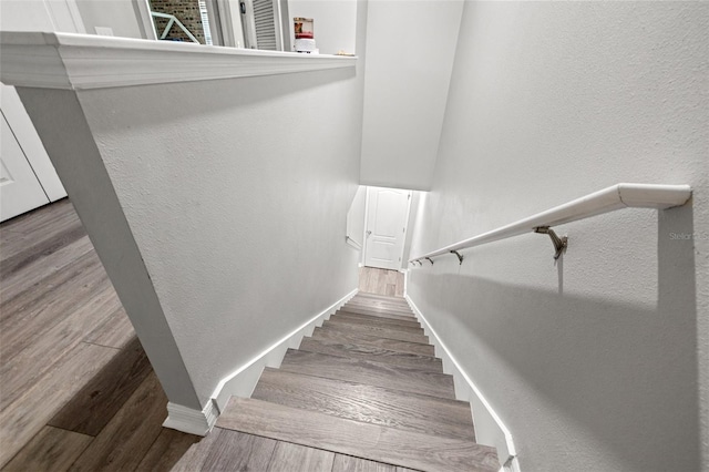 stairs with a textured wall, baseboards, and wood finished floors