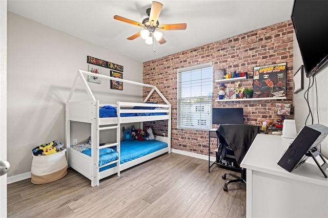 bedroom featuring wood finished floors, baseboards, brick wall, and ceiling fan