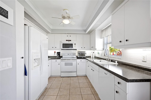 kitchen with dark countertops, a tray ceiling, decorative backsplash, white appliances, and a sink