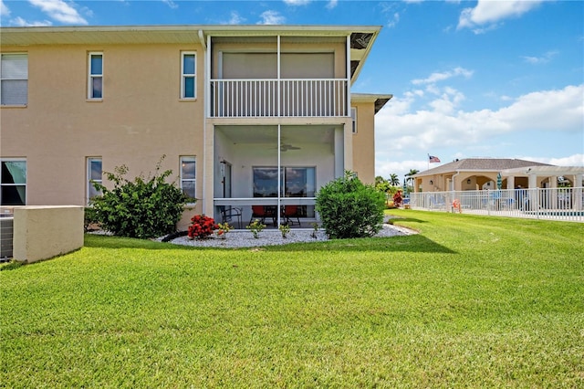 rear view of property featuring a yard, fence, and stucco siding