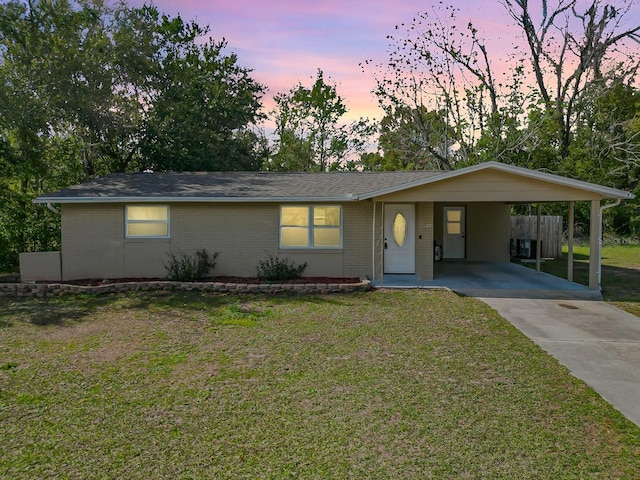 ranch-style house with a yard, an attached carport, brick siding, and driveway