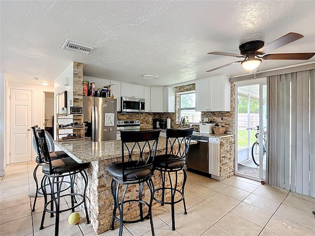 kitchen with visible vents, stainless steel appliances, light tile patterned flooring, a breakfast bar area, and decorative backsplash