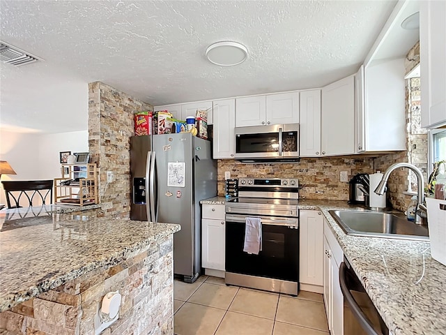 kitchen featuring light tile patterned floors, a sink, decorative backsplash, stainless steel appliances, and white cabinets