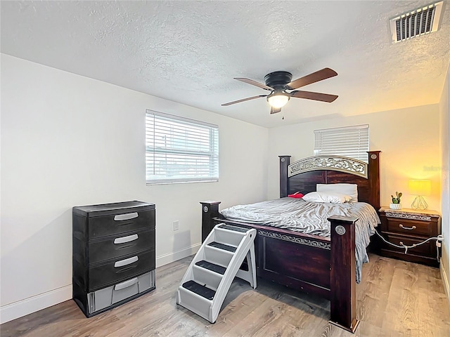 bedroom with visible vents, light wood-style flooring, a ceiling fan, a textured ceiling, and baseboards