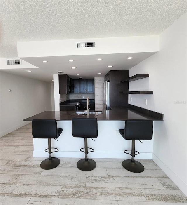 kitchen with dark countertops, visible vents, a breakfast bar area, and freestanding refrigerator