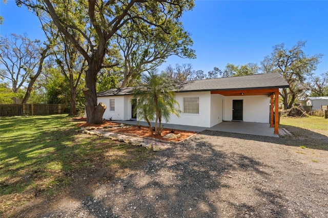 rear view of house featuring stucco siding, driveway, fence, a yard, and an attached carport