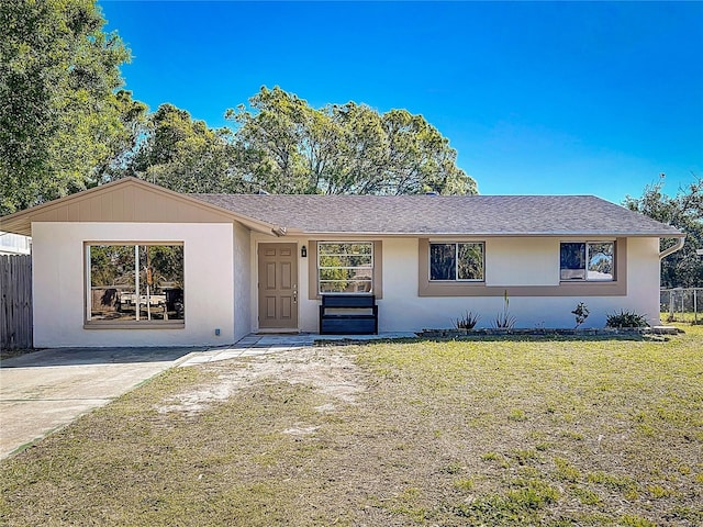 ranch-style home with a shingled roof, a front lawn, fence, and stucco siding