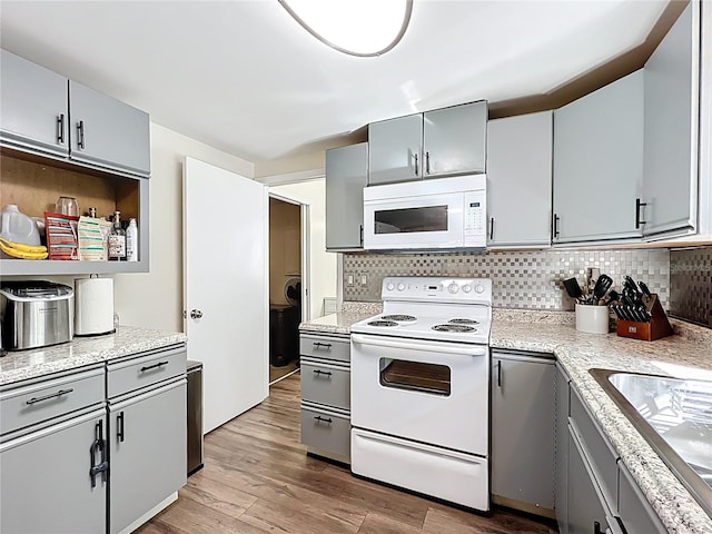 kitchen with white appliances, wood finished floors, a sink, gray cabinetry, and tasteful backsplash