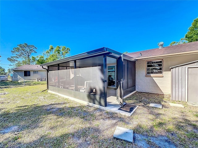 view of home's exterior with a storage unit, stucco siding, fence, a yard, and a sunroom