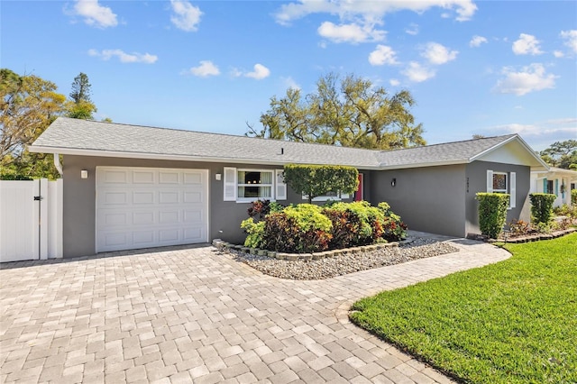 ranch-style house with stucco siding, decorative driveway, fence, a front yard, and an attached garage