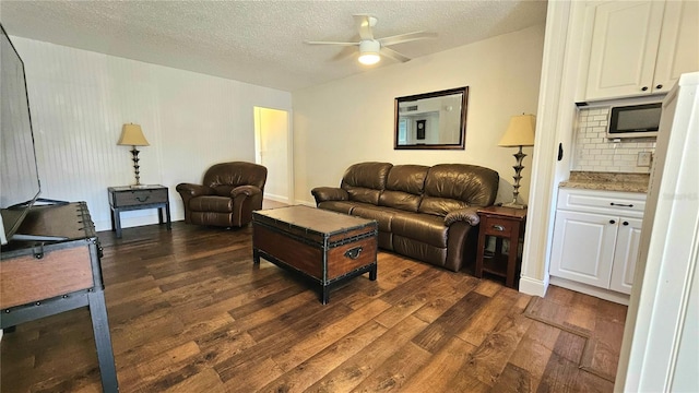 living room featuring a textured ceiling, ceiling fan, and dark wood-style flooring