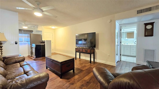 living area with a ceiling fan, wood finished floors, visible vents, and a textured ceiling