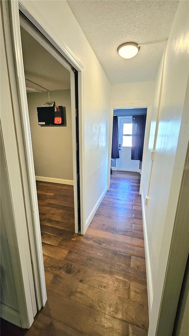 corridor with baseboards, a textured ceiling, and wood finished floors