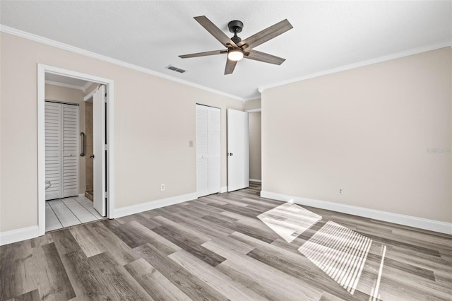 unfurnished bedroom with visible vents, wood finished floors, crown molding, baseboards, and ceiling fan