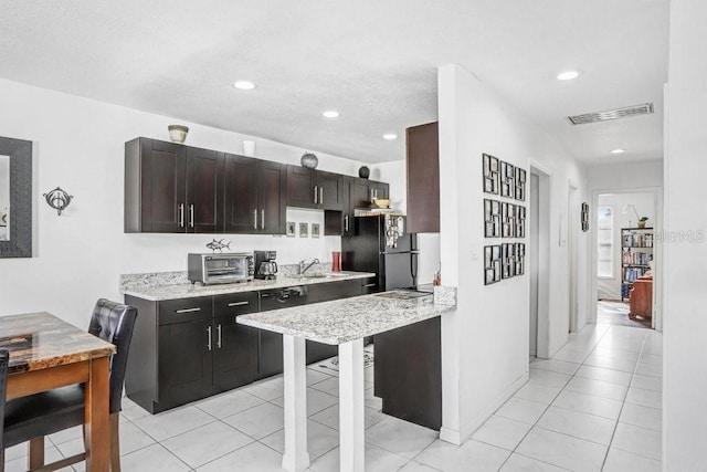 kitchen featuring visible vents, light stone countertops, a toaster, light tile patterned floors, and freestanding refrigerator