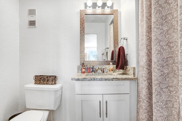 full bath with visible vents, toilet, vanity, and a textured wall