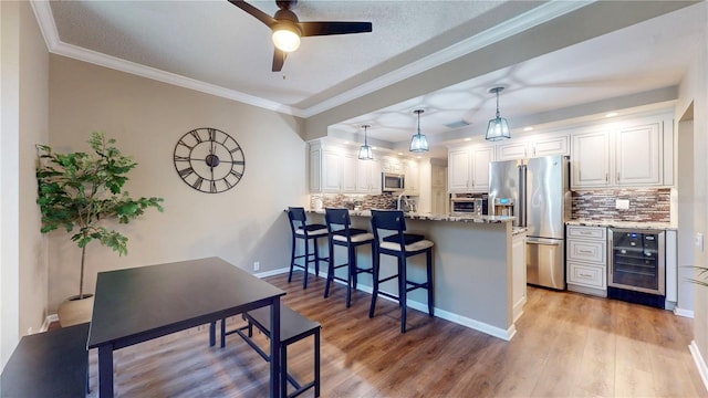 kitchen featuring a breakfast bar area, beverage cooler, a peninsula, white cabinets, and appliances with stainless steel finishes