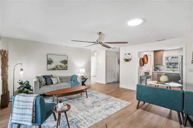 living room featuring light wood-style flooring, a ceiling fan, visible vents, and baseboards