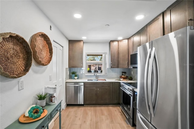 kitchen featuring light wood-type flooring, a sink, appliances with stainless steel finishes, light countertops, and decorative backsplash