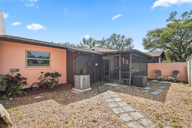 rear view of house featuring stucco siding, fence, and a sunroom